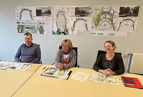 Ralf Hoppe, Andrea Stegmann und Imme Lindemann sitzen an einem Tisch, im Hintergrund an der Wand hängen die Pläne des Siegerentwurfs.n 