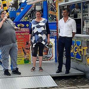 Bürgervorsteher Markus Müller läutet vor einem Fahrgeschäft eine Glocke zur Eröffnung. Neben ihm Marktmeisterin Nina Kramer und Bürgermeister Ralf Hoppe.