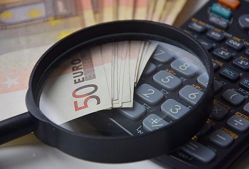 Eine Lupe liegt auf einem Taschenrechner und aufgefächerten 50-Euro-Scheinen