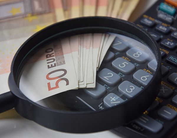 Eine Lupe liegt auf einem Taschenrechner und aufgefächerten 50-Euro-Scheinen