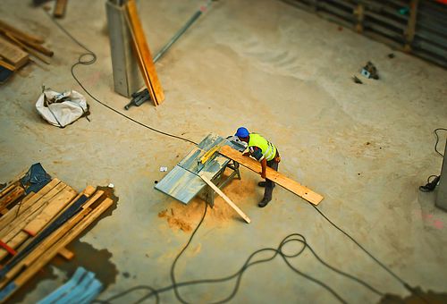 Ein Bauarbeiter auf einer Baustelle steht an der Kreissäge und sägt ein Brett.