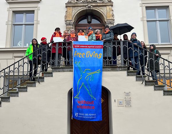 Mitglieder des Frauennetzwerks Steinburg stehen auf der Empore des Historischen Rathauses, von der die Flagge "Frei leben ohne Gewalt" herunterhängt.  