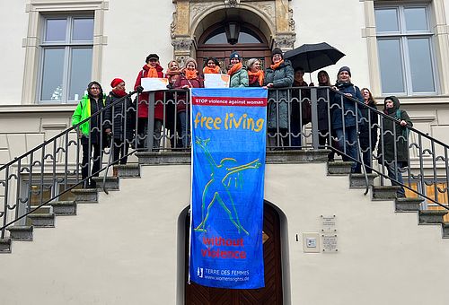 Mitglieder des Frauennetzwerks Steinburg stehen auf der Empore des Historischen Rathauses, von der die Flagge "Frei leben ohne Gewalt" herunterhängt.  