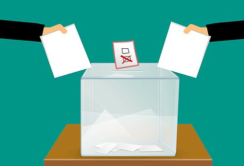 Hände stecken zwei Wahlzettel in eine Urne.